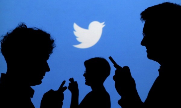 Pessoas no celular com a logo do twitter atrás